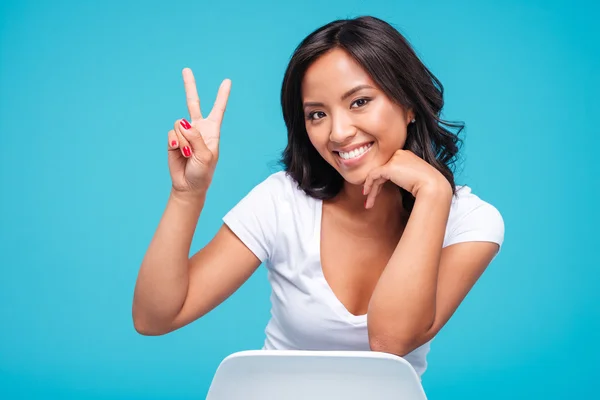 Woman sitting on the chair and showing victory sign — Stockfoto