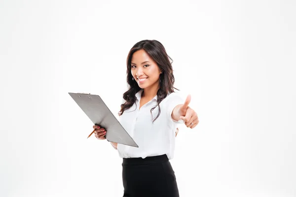 Amistosa joven mujer de negocios sonriente con portapapeles mostrando los pulgares hacia arriba gesto —  Fotos de Stock