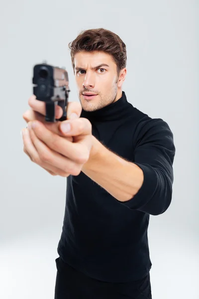 Koncentruje się młody człowiek, stojąc i wskazując z pistoletu na Ciebie — Zdjęcie stockowe