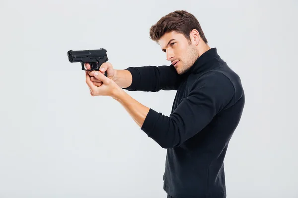 Konzentrierter junger Mann steht und zielt mit Waffe — Stockfoto