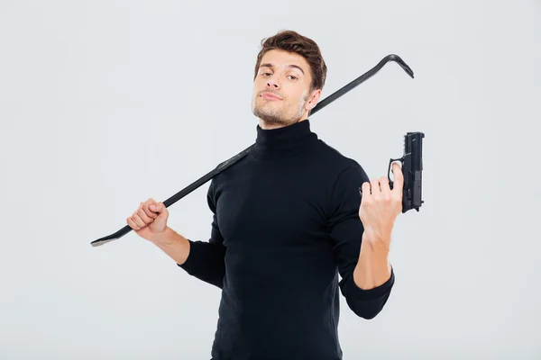 Selbstbewusster junger Mann Einbrecher posiert mit Waffe und Brechstange — Stockfoto