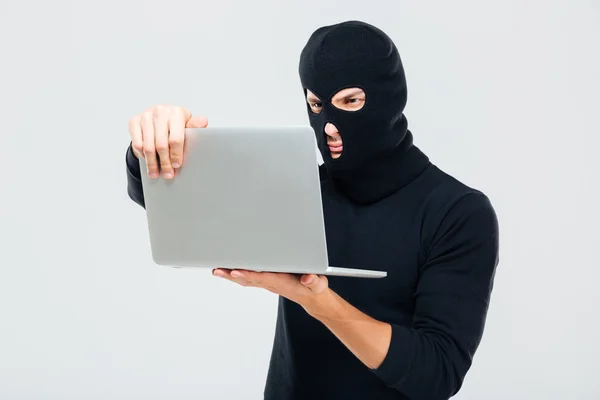 Krimineller junger Mann mit Sturmhaube steht und benutzt Laptop — Stockfoto