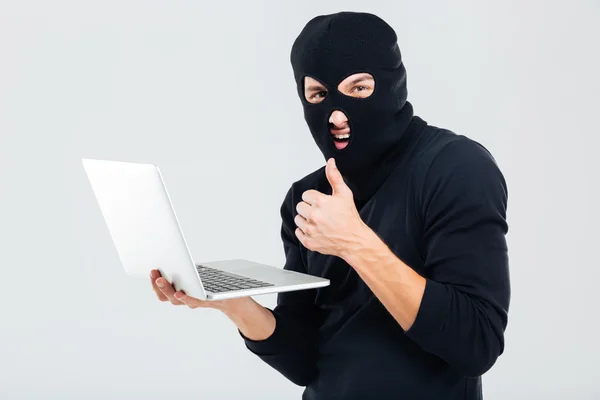 Homem em balaclava usando laptop e mostrando os polegares para cima — Fotografia de Stock