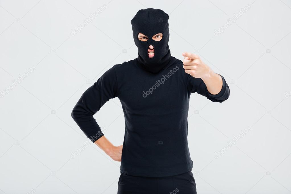 Mad irritated man in balaclava standing and pointing on you