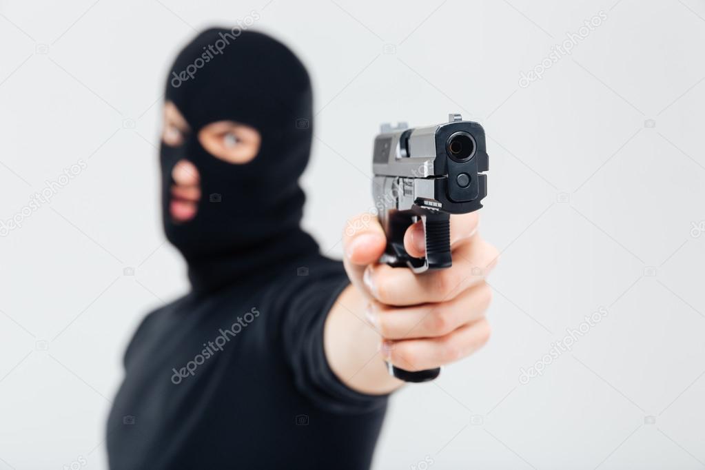 Man robber in balaclava pointing with gun