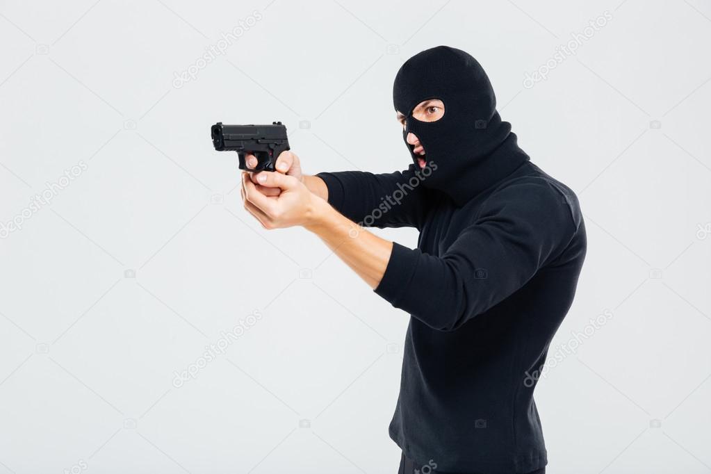 Criminal man in balaclava standing and aiming with gun