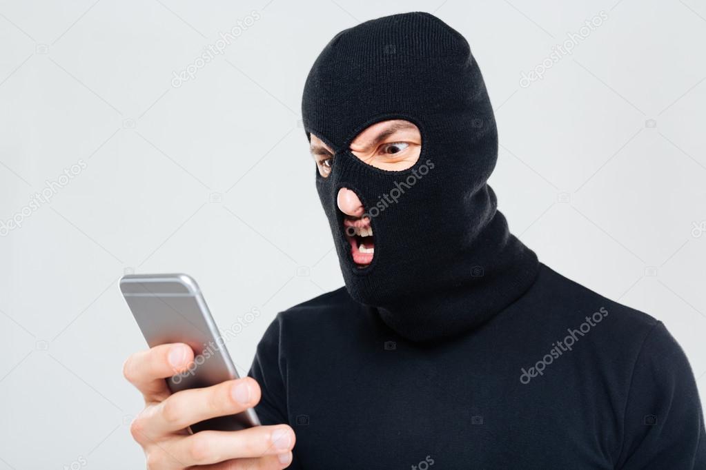 Mad aggressive man in balaclava standing and using mobile phone
