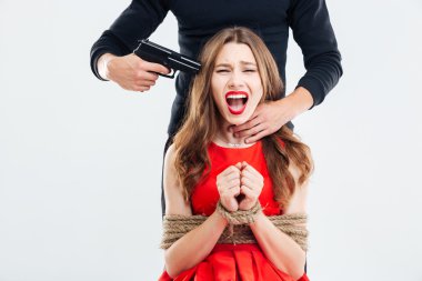 Woman sitting bounded using ropes threatened by man with gun clipart