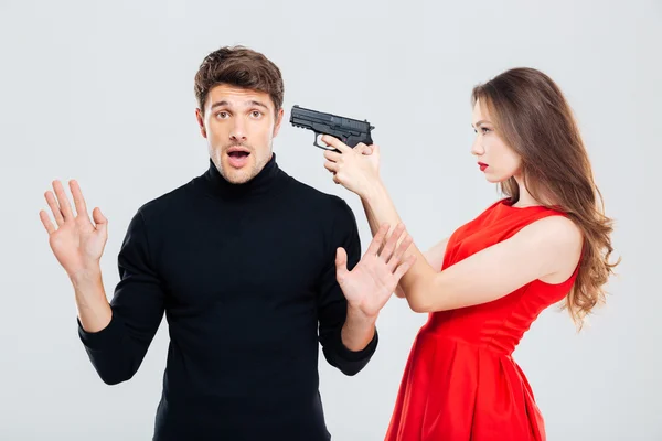Женщина, стоящая и угрожающая пистолетом напуганному молодому человеку — стоковое фото