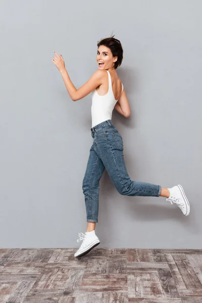 Весела красива дівчина стрибає на сірому фоні — стокове фото