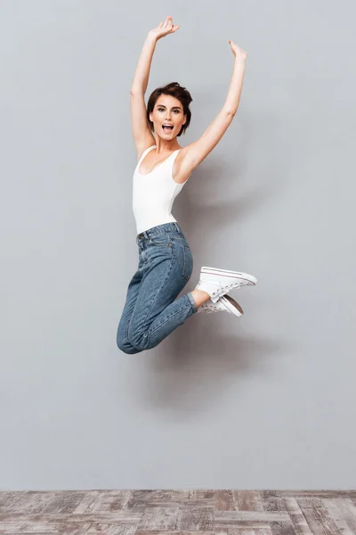 Glad söt flicka hoppar över grå bakgrund — Stockfoto