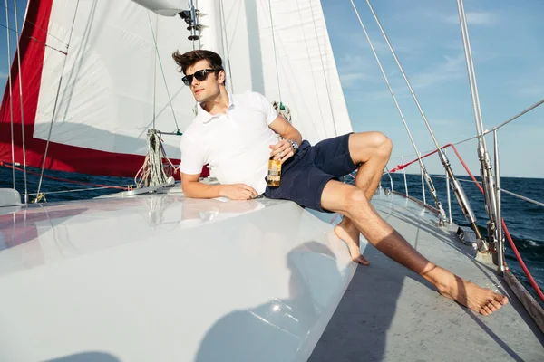 Bello giovane che beve birra mentre riposa sullo yacht — Foto Stock