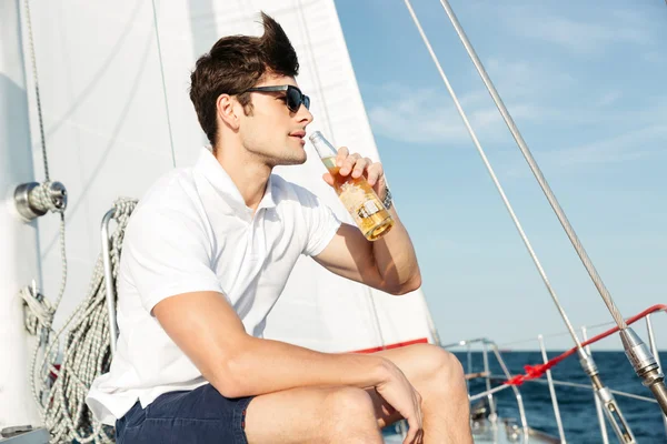 Bello giovane che beve birra mentre riposa sullo yacht — Foto Stock
