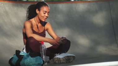 Güzel bir Afrikalı Amerikalı genç kadın akıllı telefonunu kullanıyor. Sabahları dışarıda bir spor salonunda oturuyor.