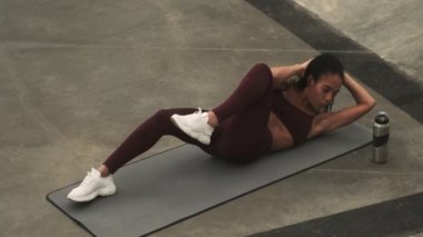 Zayıf, genç bir Afrikalı Amerikalı kadın spor sahasındaki yoga minderinde egzersiz yapıyor.