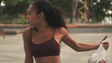 Kulaklık takan odaklanmış genç bir Afrikalı Amerikalı kadın spor sahasında yoga minderinde esneme egzersizleri yapıyor.