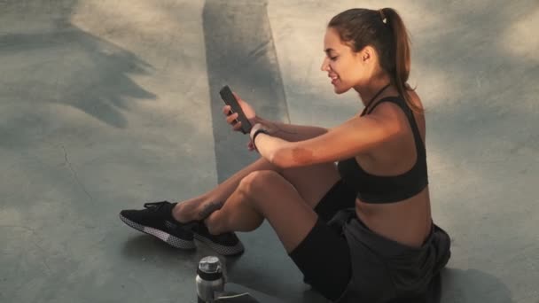 매력적 여성이 스포츠 경기장에 스마트폰으로 자신의 스마트 워치를 연결하고 있습니다 — 비디오