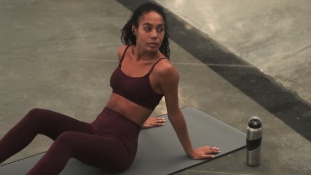 一位穿着运动服 从容的年轻非洲女子正坐在运动场上的瑜伽垫上 — 图库视频影像
