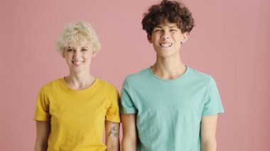 Gülümseyen adam ve kadın pembe arka planda başparmak hareketi yapıyorlar.