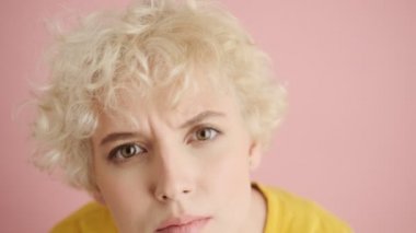 Ciddi sarışın genç bir kadının yakın plan görüntüsü pembe arka planda tek başına duran bir şeyi dikizliyor.