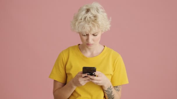 Egy Elégedetlen Szőke Fiatal Használja Okostelefonját Elszigetelve Áll Rózsaszín Háttér — Stock videók