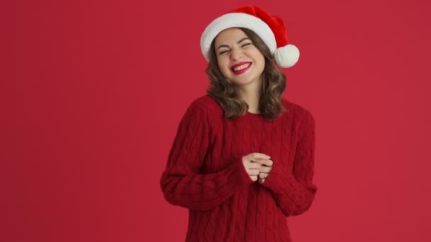 暖かい赤いセーターとクリスマスの帽子を身に着けている夢の女性は赤い背景に隔離されて立っています — ストック動画