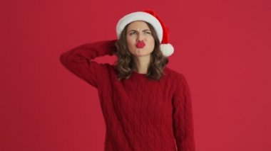Sıcak kırmızı kazak ve Noel şapkası giyen mutlu bir kadın kırmızı arka planda izole edilmiş bir fikirle geliyor.