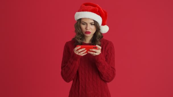 빨간색 스웨터를 크리스마스 모자를 그녀의 스마트폰에서 게임을 여성이 있습니다 — 비디오