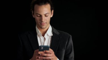 Siyah arka planda izole edilmiş cep telefonu kullanan takım elbiseli yakışıklı bir adam.