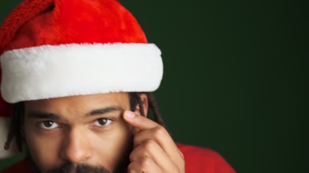 年轻快乐快乐的非洲男人戴着圣诞圣塔帽 触摸着绿墙背景上的胡子 — 图库视频影像