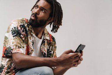 Gri duvar arka planında cep telefonu kullanan şok olmuş Afrikalı bir adamın görüntüsü