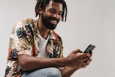 Gri duvar arka planında cep telefonu kullanan pozitif gülümseyen Afrikalı bir adamın görüntüsü