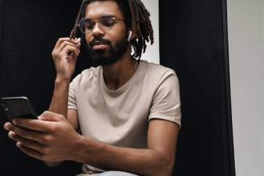 Afrikalı ciddi bir adamın fotoğrafı, kulaklıkla müzik dinlerken cep telefonu kullanarak siyah ve beyaz arka plan üzerinde izole edilmiş.