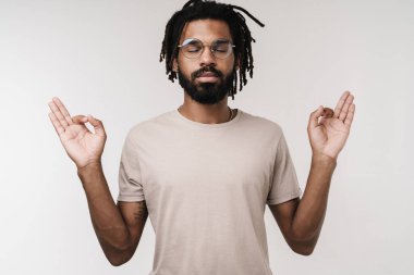 Gözlüklü, gri duvar arkaplanından izole edilmiş, konsantre meditasyon yapan Afrikalı adam görüntüsü.