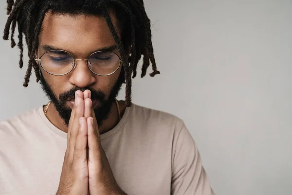 眼鏡の中の灰色の壁の背景に隔離された深刻な祈りアフリカの男のイメージ — ストック写真