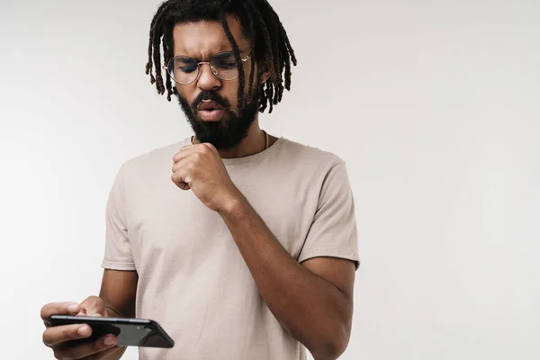 メガネで灰色の壁の背景に隔離された携帯電話でゲームをプレイする神経の負のアフリカの男のイメージ — ストック写真