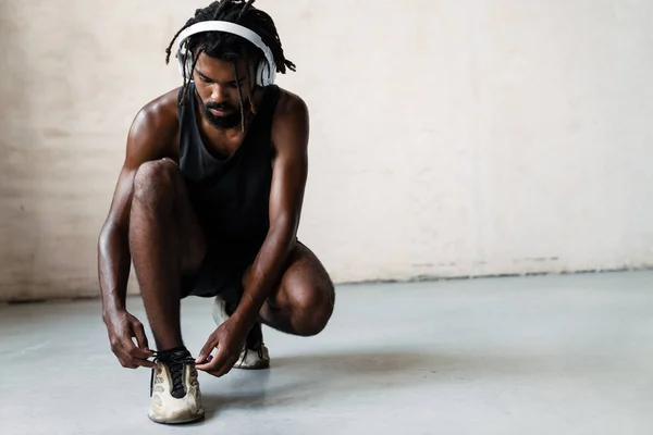 屋内で作業しながら 彼の靴ひもを結ぶヘッドフォンでアフリカ系アメリカ人のスポーツマンのイメージ — ストック写真