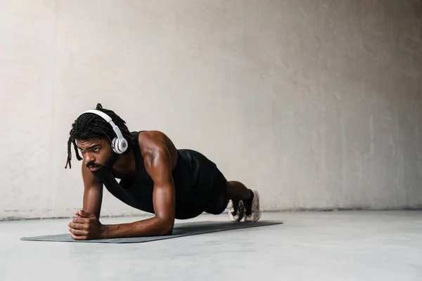 屋内マットで作業しながら運動をするヘッドフォンで強力なアフリカ系アメリカ人スポーツマンのイメージ — ストック写真