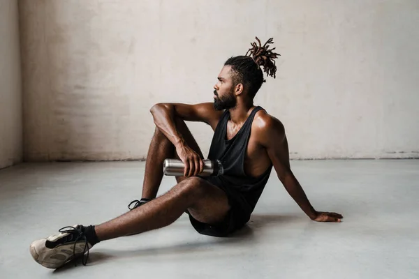 水のボトルを屋内で床に座っているアフリカ系アメリカ人スポーツマンの焦点のイメージ — ストック写真