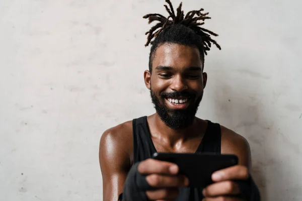图为非洲裔美国运动员站在室内用手机微笑 — 图库照片