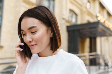 Memnun genç Asyalı bir kadının cep telefonuyla konuşurken sokakta yürümesi.