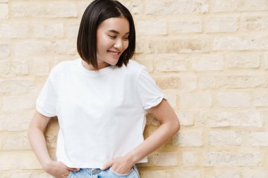 Duvarın arkasında poz veren mutlu bir Asyalı kadın resmi.