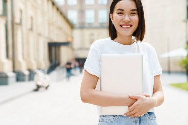 Sokakta dizüstü bilgisayarla dolaşan neşeli Asyalı genç bir kadının görüntüsü