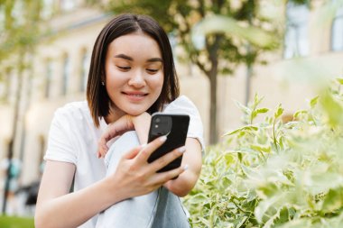 Pozitif iyimser bir Asyalı kadının açık havada cep telefonu kullanırken çekilmiş fotoğrafı.