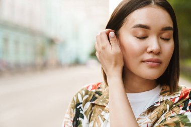 Memnun Asyalı genç bir kadının fotoğrafı. Sokakta yürüyor.