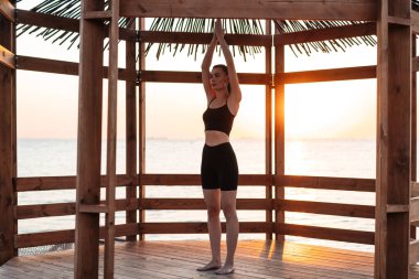 Spor kıyafetli güzel bir kızın şafak vakti bungalovda yoga egzersizi yapması.