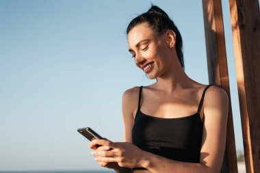 Sahilde gülümseyen ve cep telefonu kullanan genç bir kız resmi