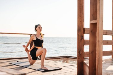 Sahilde esneme egzersizleri yapan oldukça yoğun, genç ve güzel bir fitness kadınının fotoğrafı.