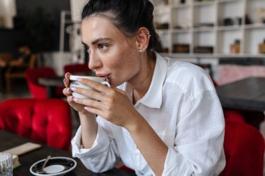 Kafede oturup kahve içen güzel, mutlu bir kadının görüntüsü.