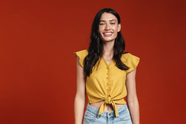 Kırmızı arka planda izole edilmiş gülümseyen ve kameraya bakan genç bir kadın görüntüsü